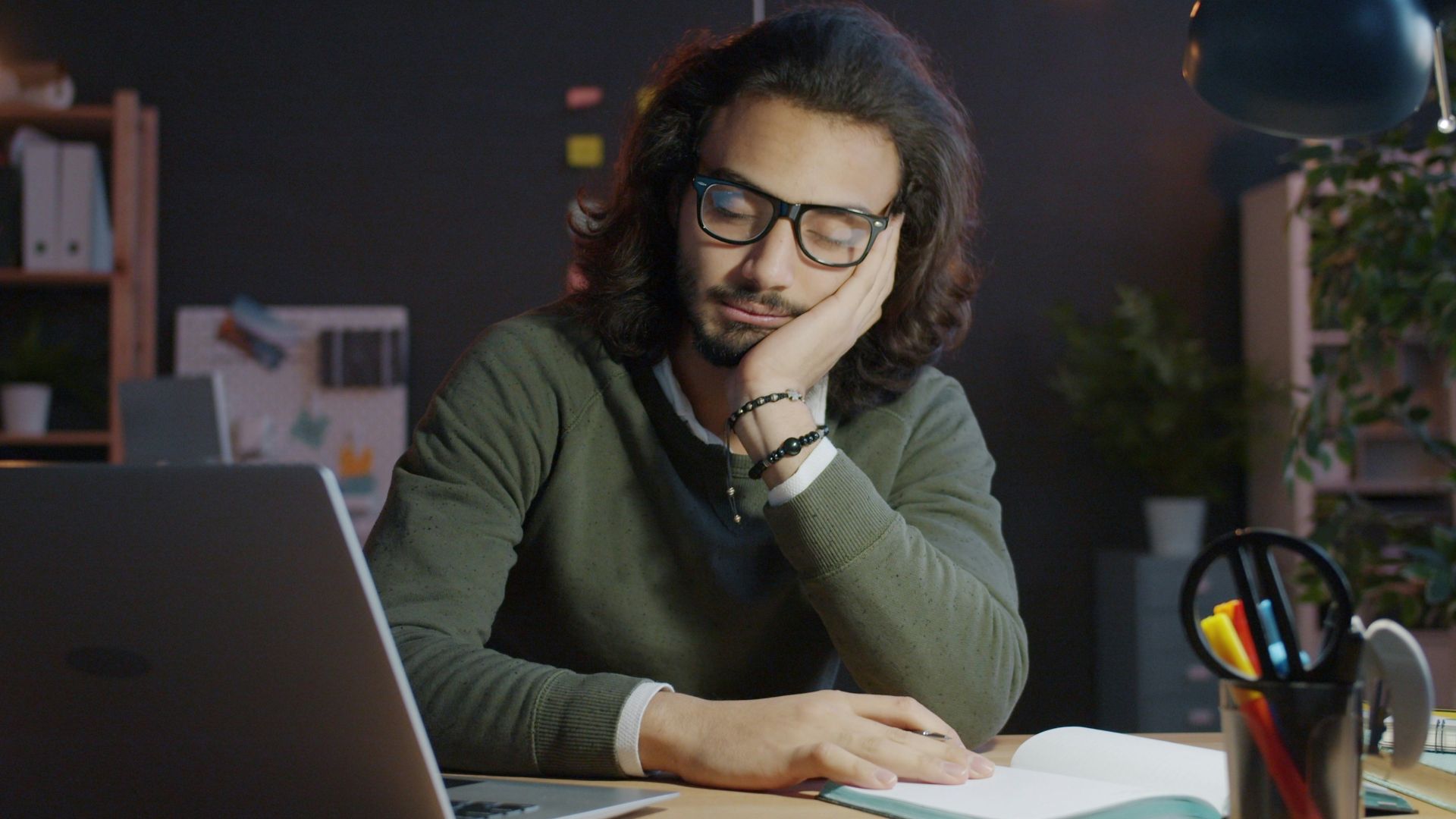 Man sleeping at desk with laptop and notebook.