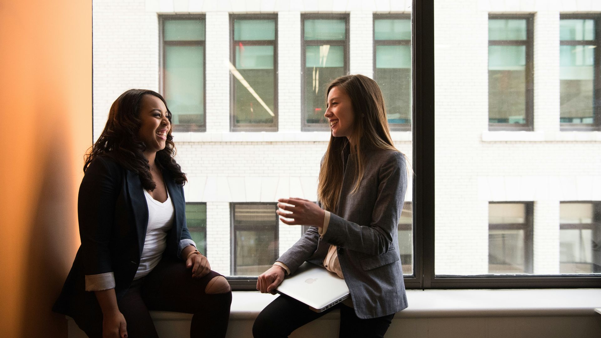 two woman sitting by the window laughing