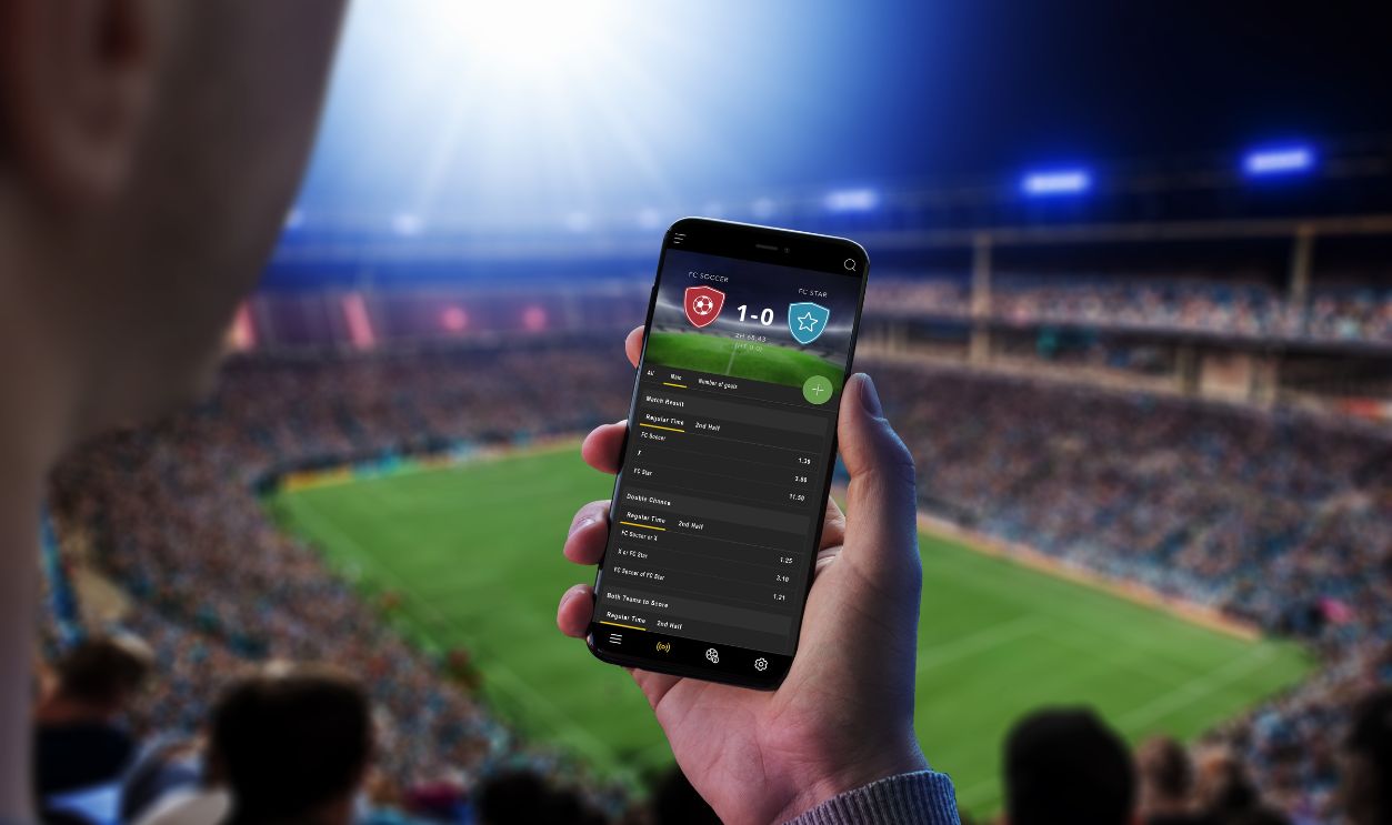 Man at a football match follows the odds and the current score. The concept of online sports betting. Football stadium and crowd in the background