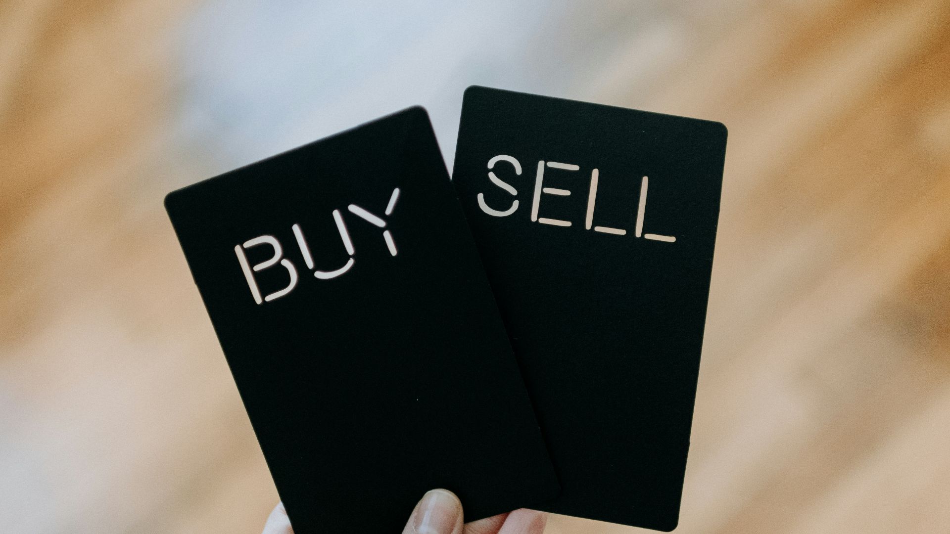 a hand holding two black cards with the words buy and sell written on them