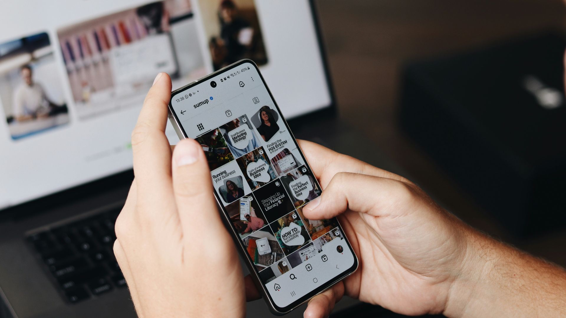 A person holding a cell phone in front of a laptop