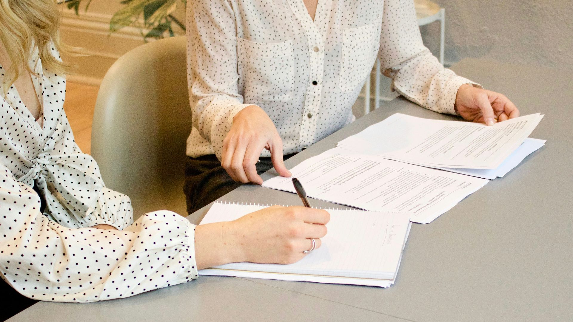 woman signing on white printer paper beside woman about to touch the documents