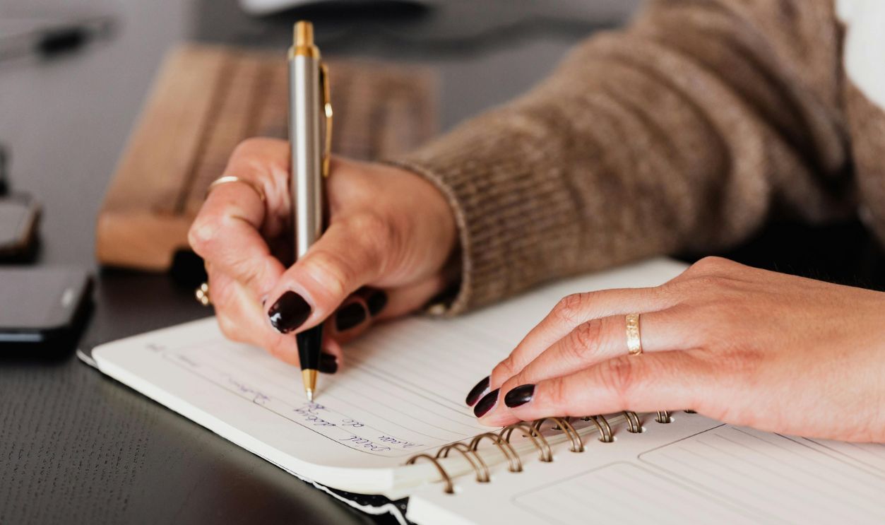 Crop woman writing down notes in diary