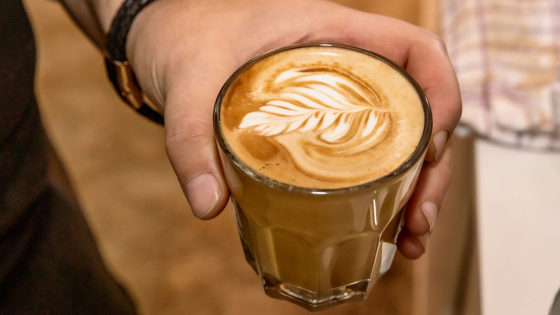 person holding clear drinking glass with brown and white liquid