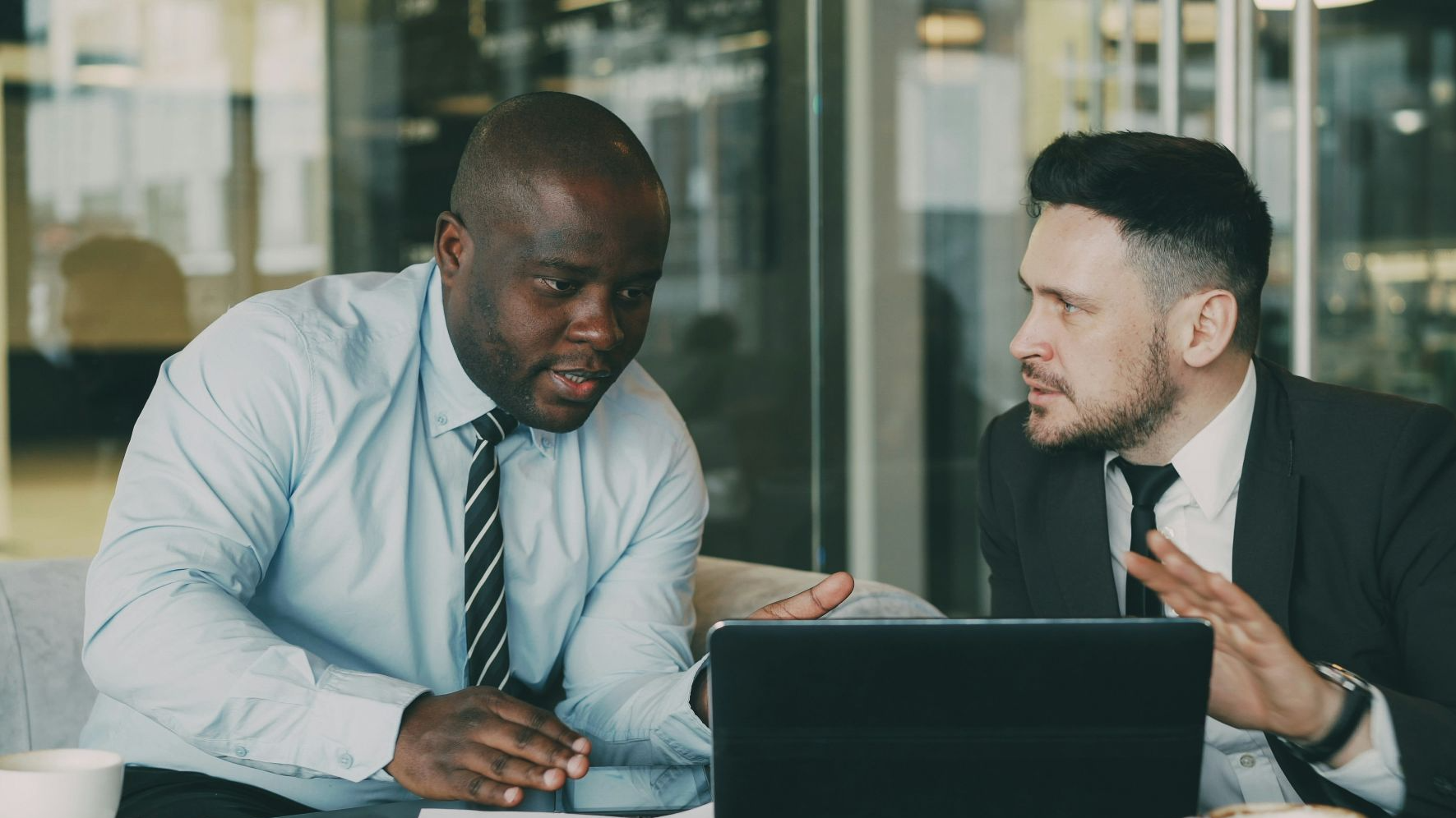 Two businessmen collaborating over a tablet and laptop.