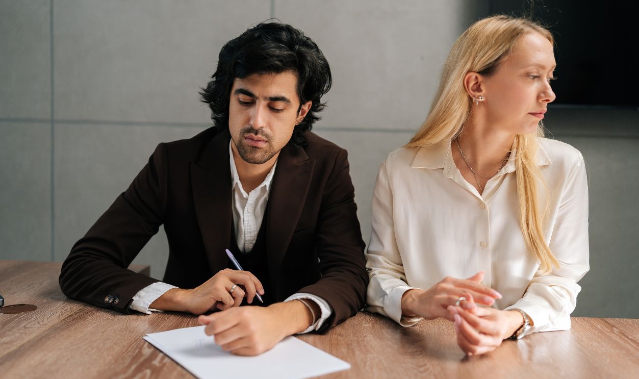 Portrait of sad spouses couple signing decree papers getting divorced in lawyers office at desk. Unhappy married man and woman filing divorce, shares or mortgage assets with attorney.