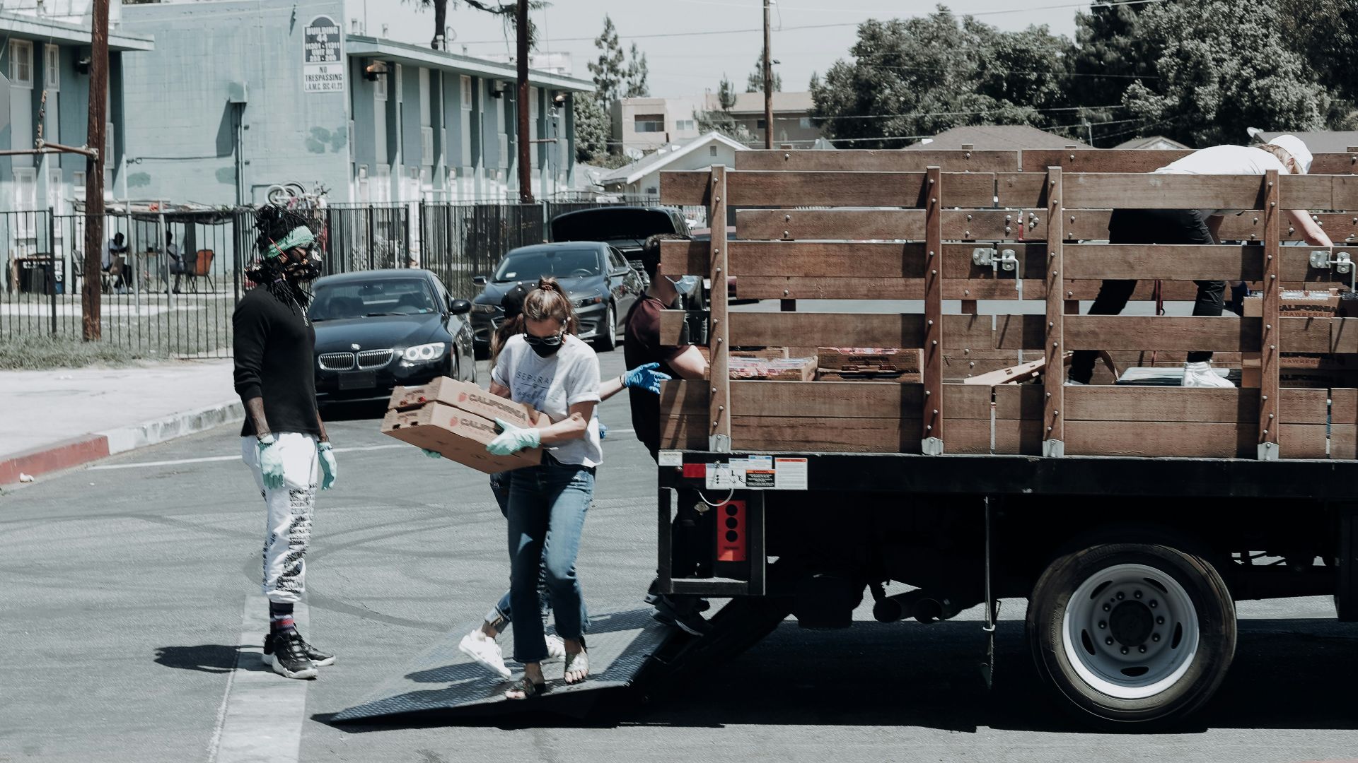 man in black jacket and blue denim jeans standing beside brown wooden box trailer during daytime
