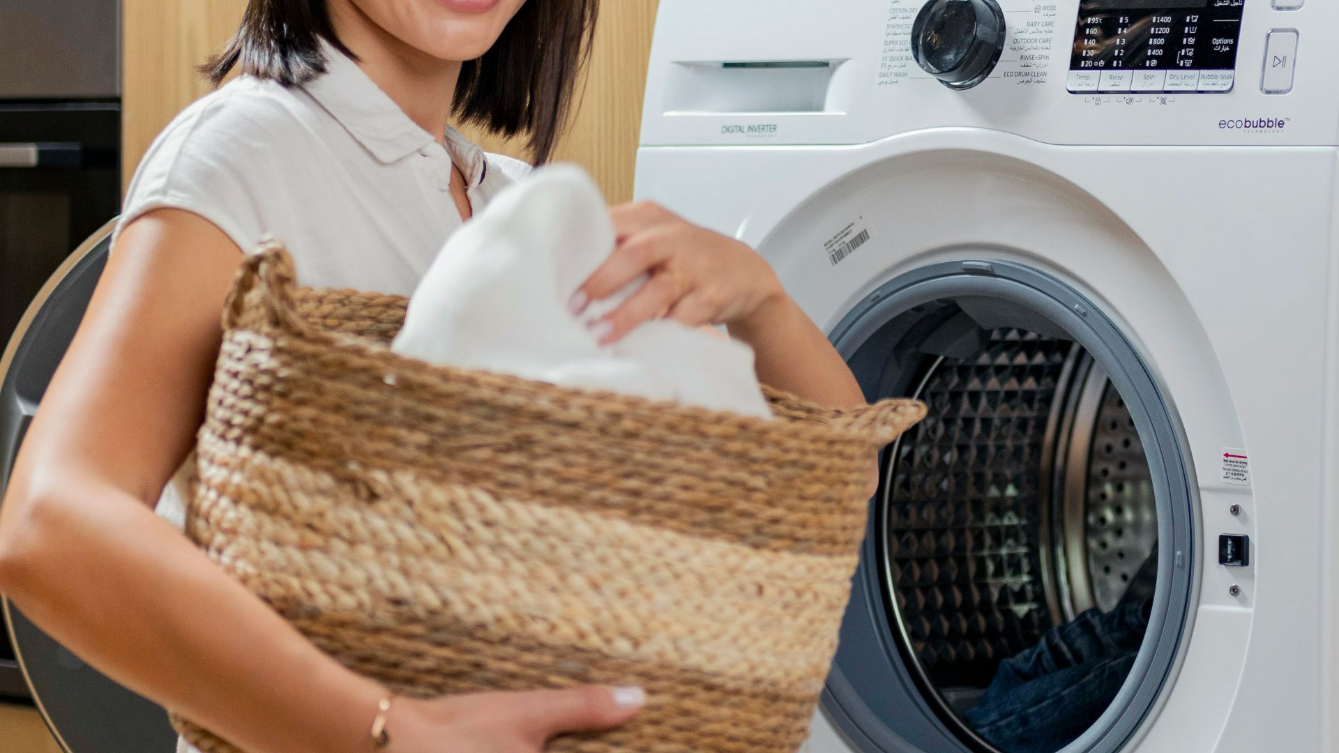 a woman is holding a basket near a washing machine