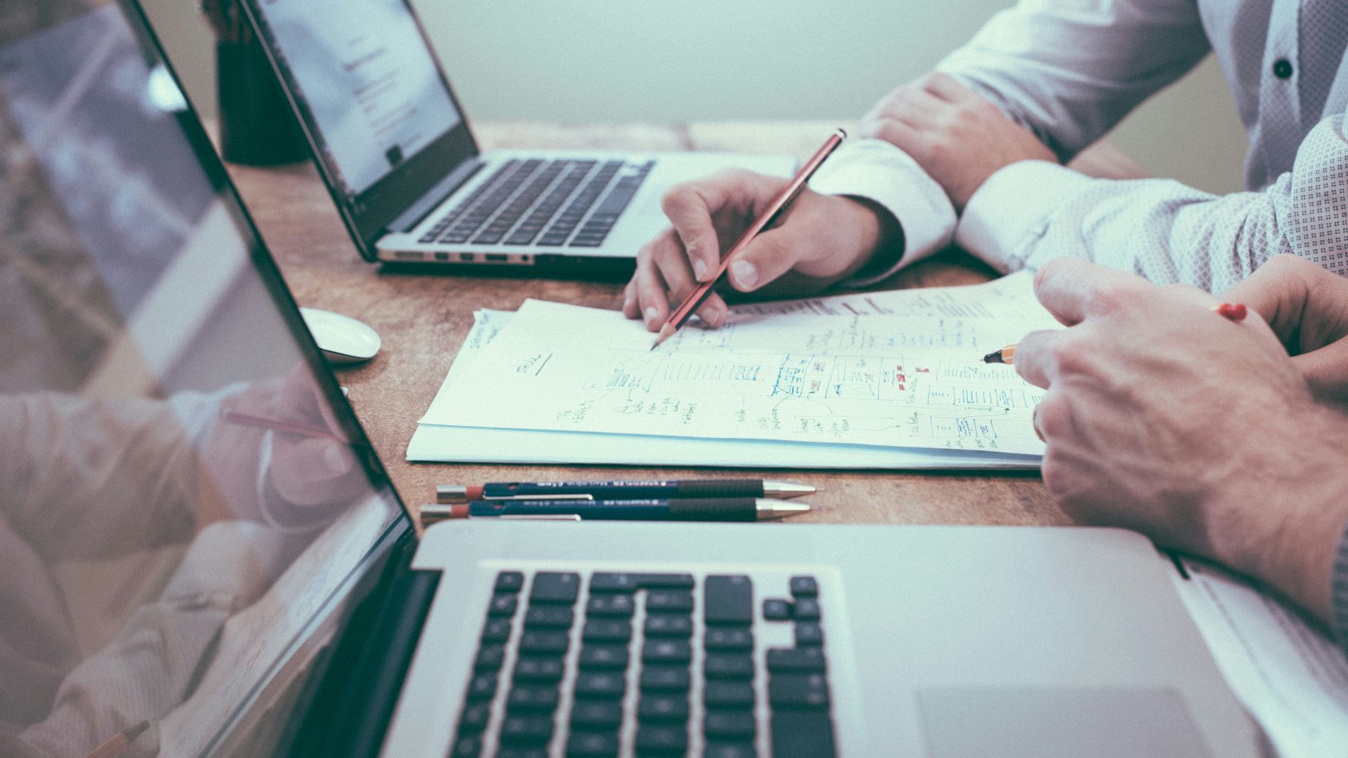 person holding pencil near laptop computer