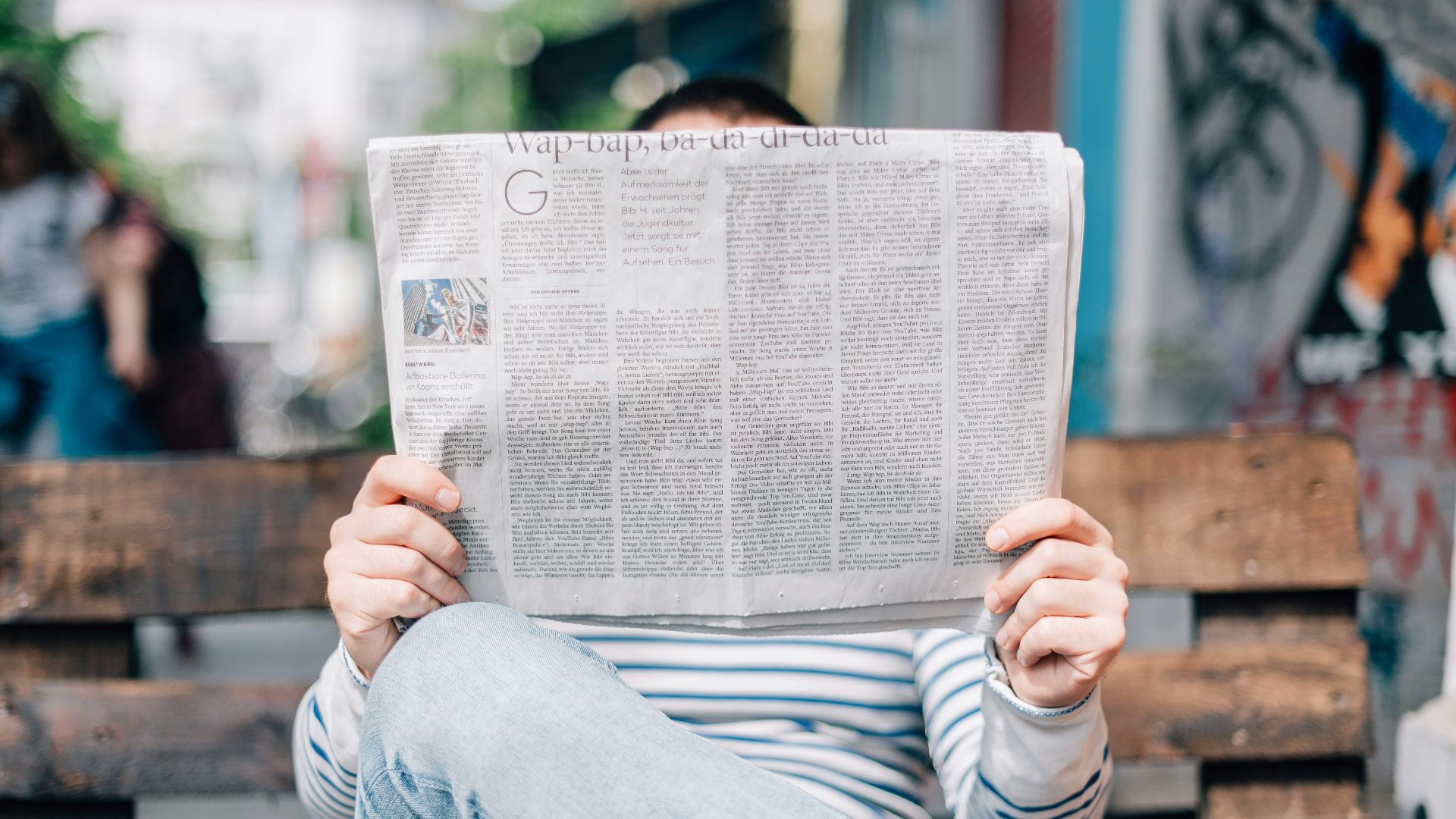 man sitting on bench reading newspaper