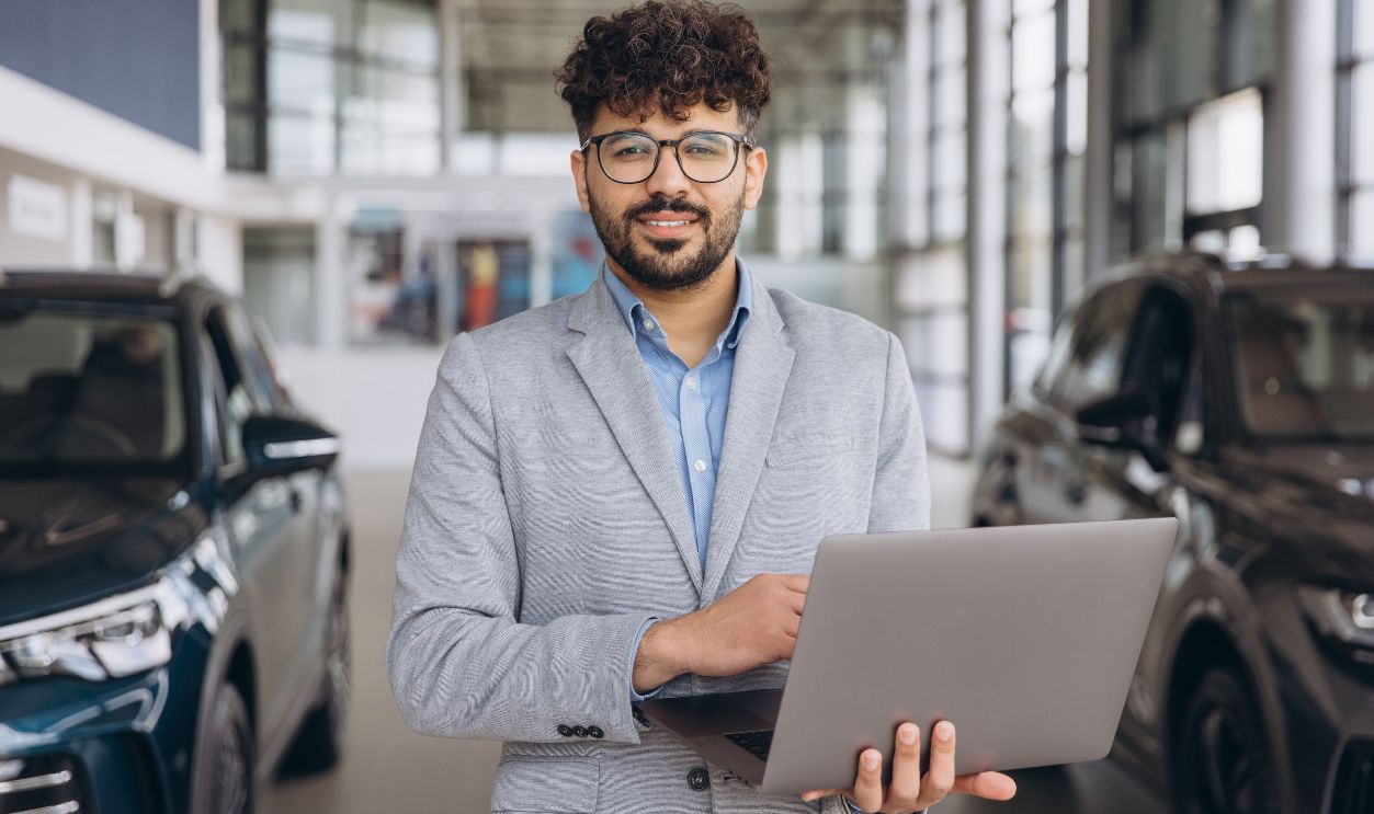 Salesperson using laptop in dealership showroom, offering professional assistance and expertise to potential customers