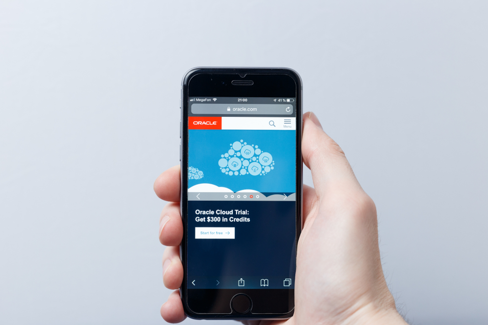 A hand holding a smartphone which displays Oracle Corporation logo on the official website homepage.
