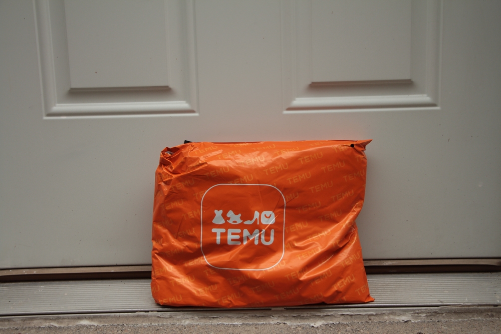 Temu orange rectangle bag package with logo on it delivery delivered leaning against white door.