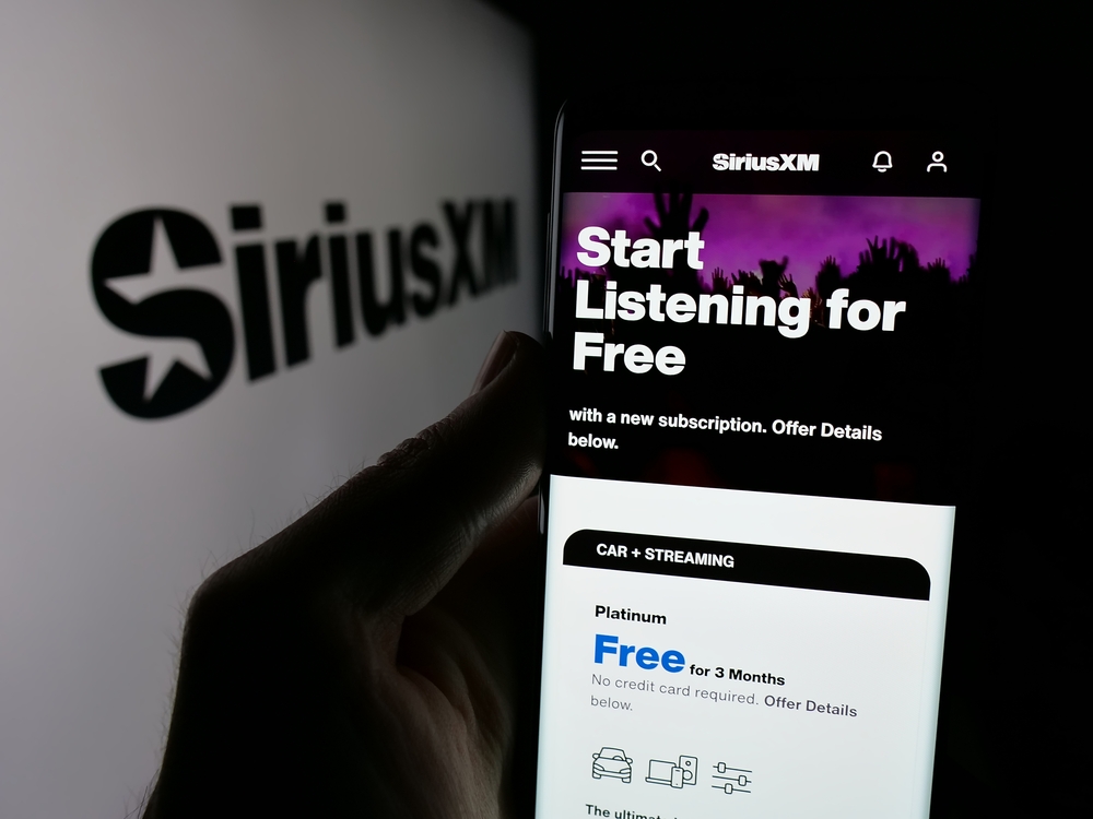 Person holding cellphone with webpage of US broadcasting company Sirius XM Holdings Inc. on screen with logo.