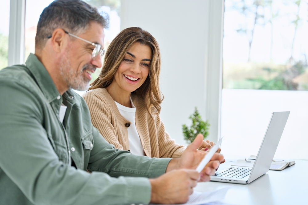 Happy middle aged couple using laptop, setting money for retirement