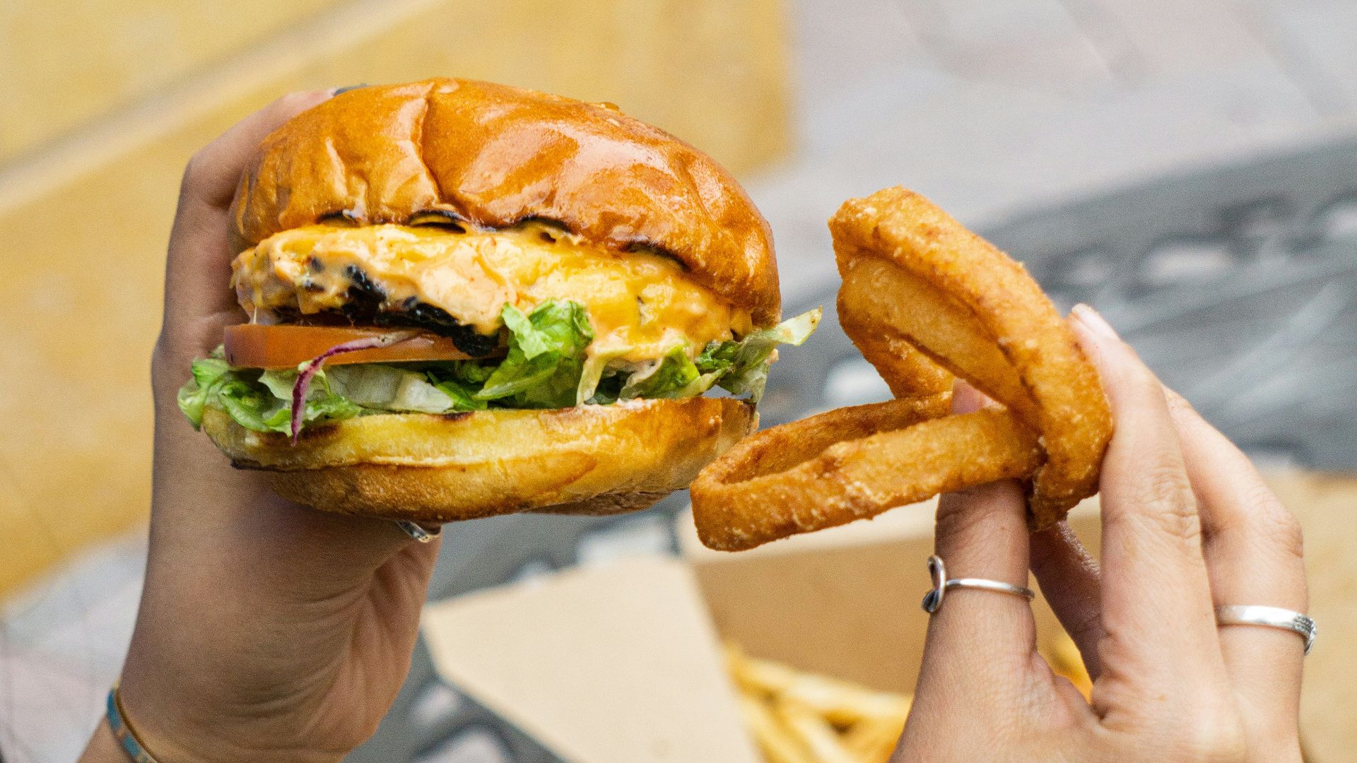 person holding burger with lettuce and tomato