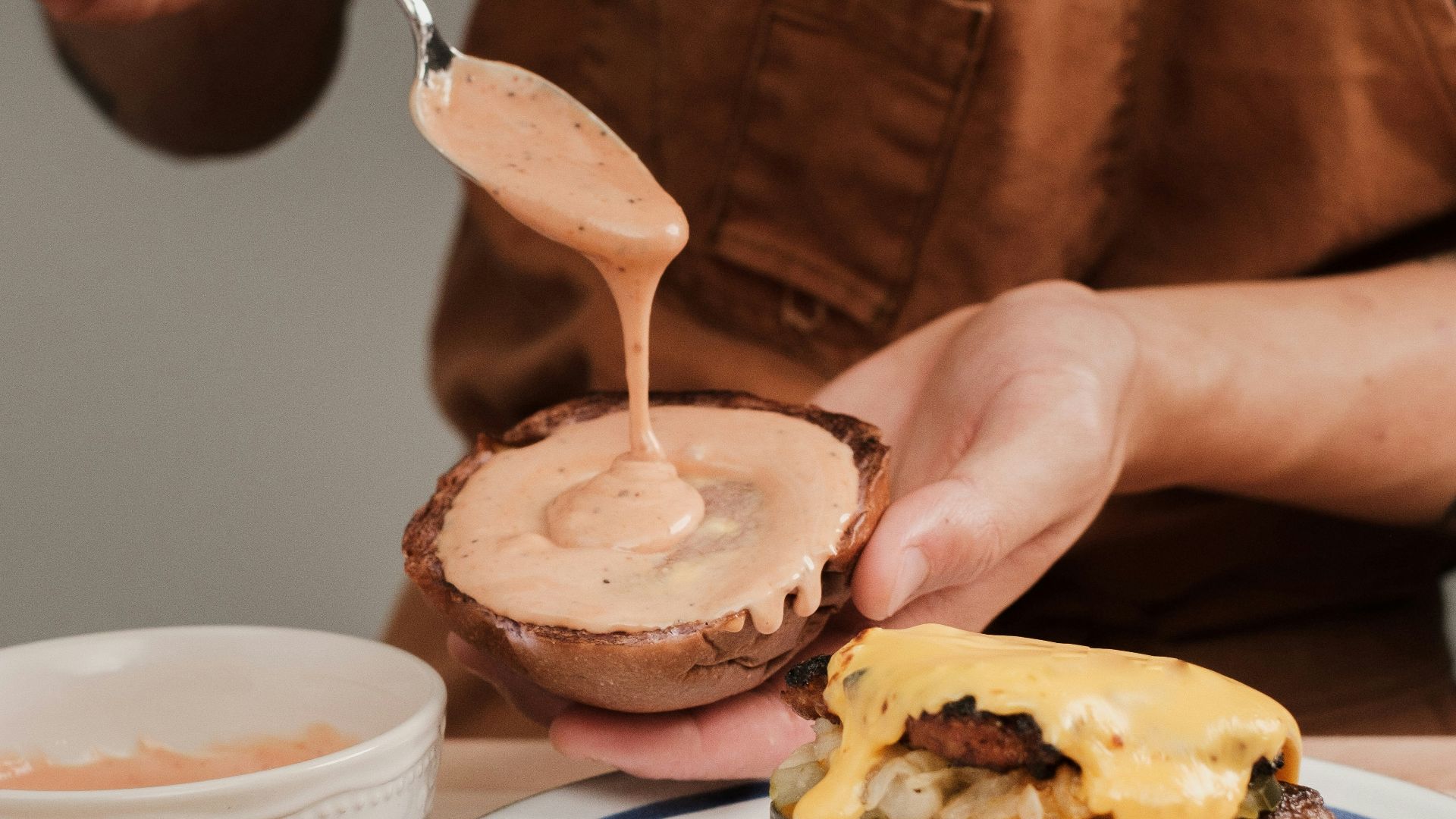 a person is spreading sauce on a hamburger