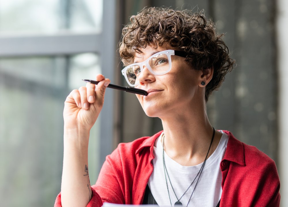 Young pensive female in eyeglasses thinking of new creative ideas