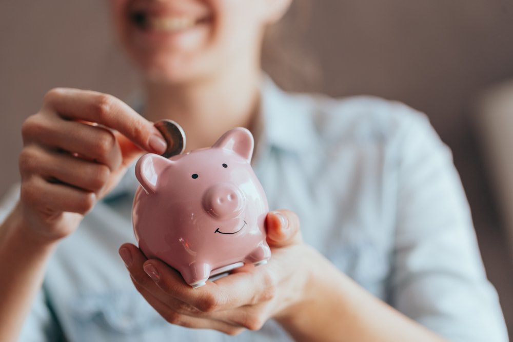 Female hands hold a pink piggy bank and puts a coin there