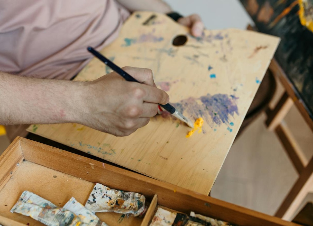 A Person Mixing Colors on a Wooden Board with a Paint Brush