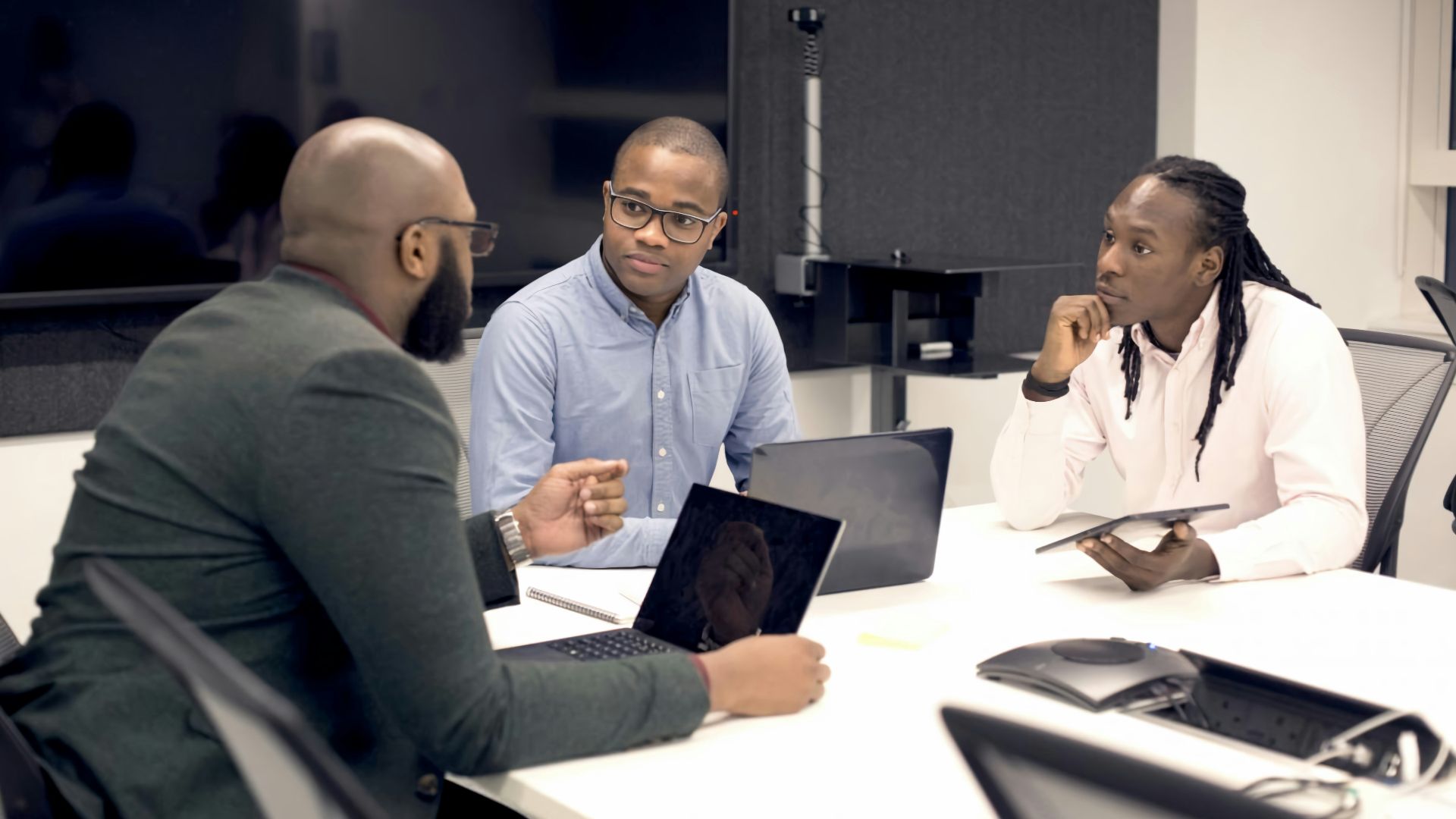 a group of people sitting around a table with laptops