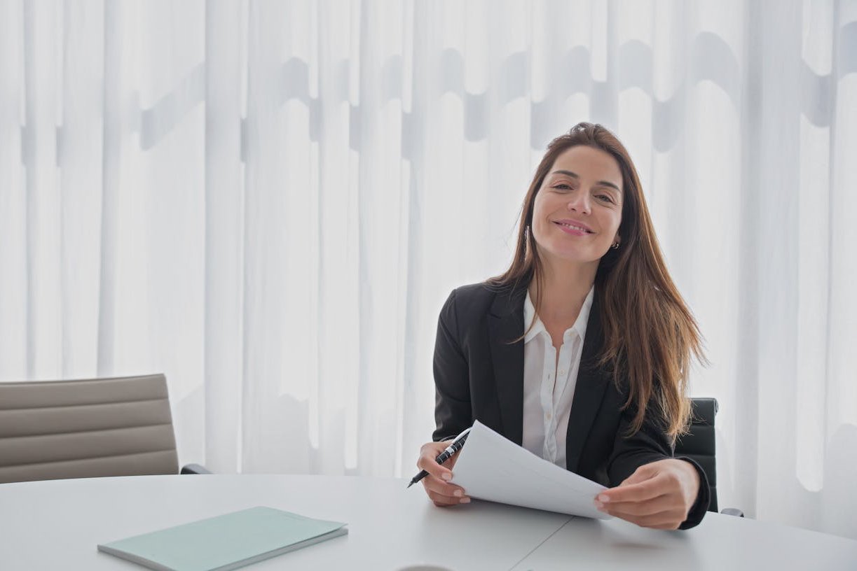 Woman Smiling in Black Blazer Holding White Paper