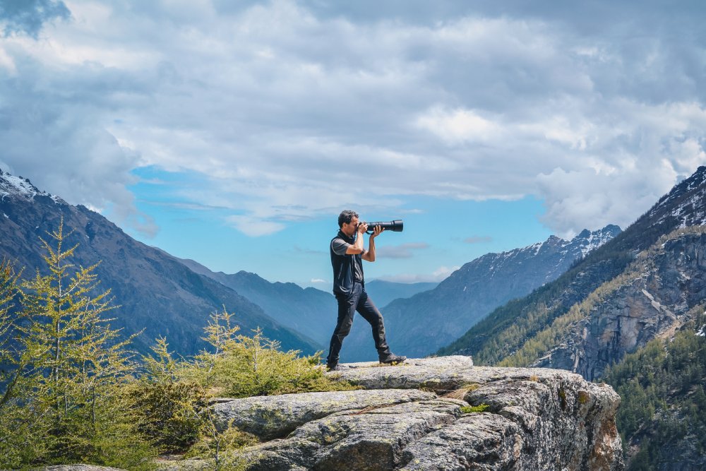Young male wildlife photographer in blue cloths taking pictures