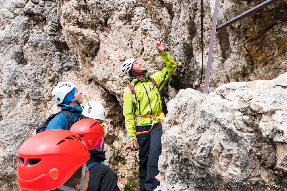 A male mountain guide instructs young climbers in the Dolomites