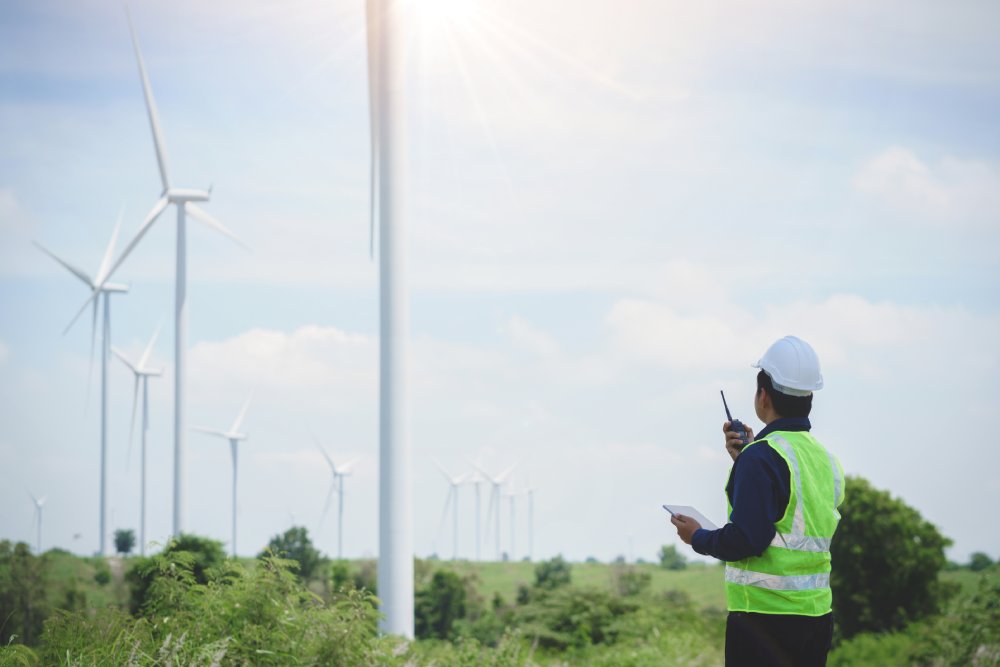 Engineer man stand holding tablet front the wind turbines generating electricity power station