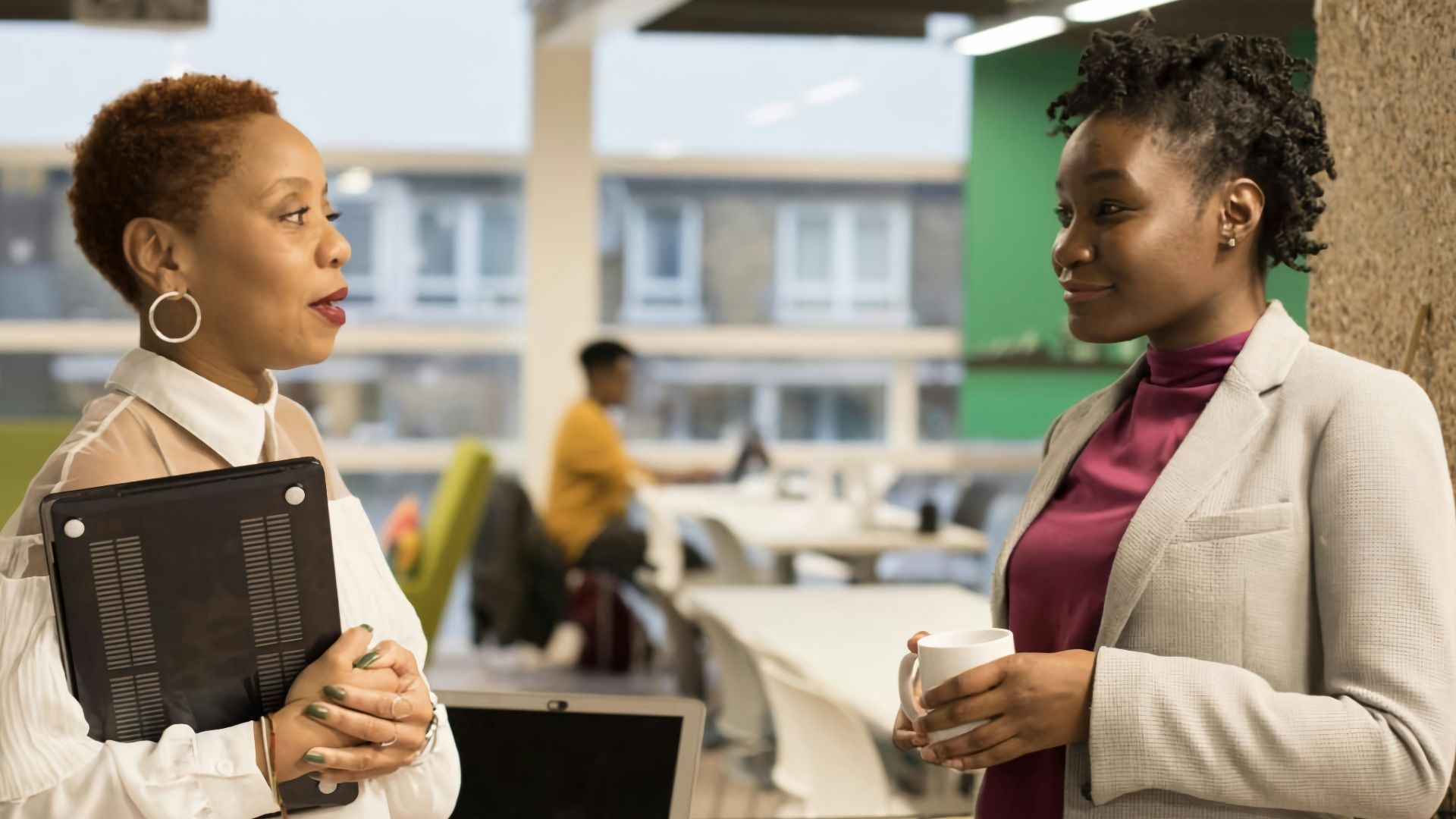 two women standing next to each other in front of a laptop