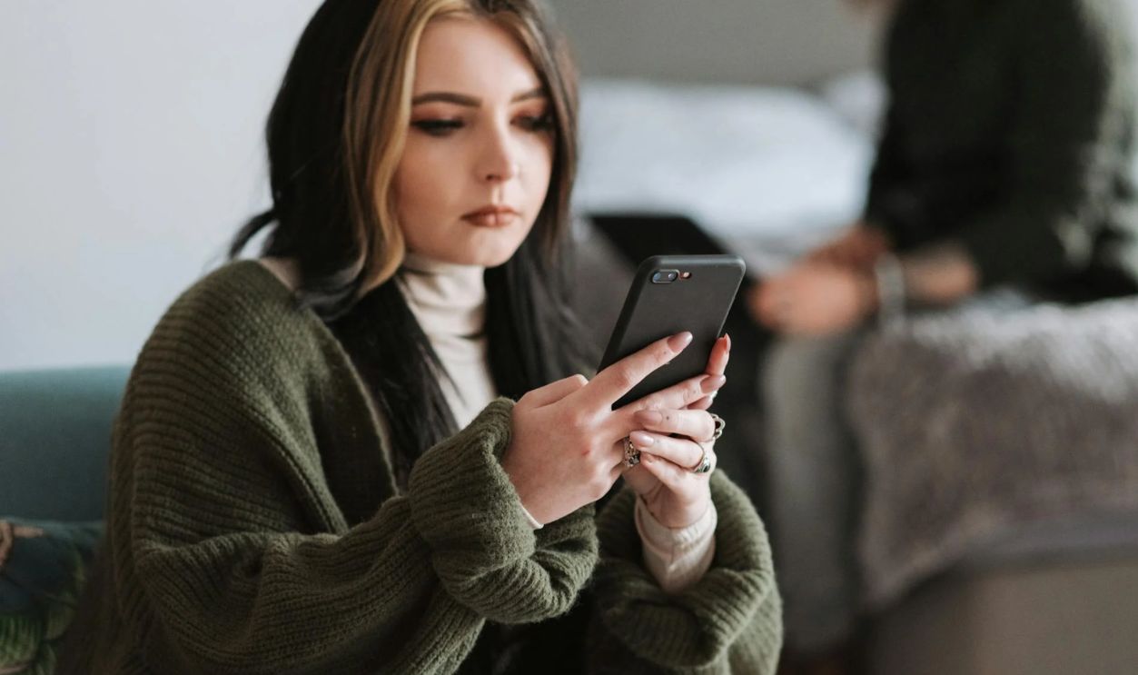 Thoughtful young woman messaging on smartphone near boyfriend typing on netbook