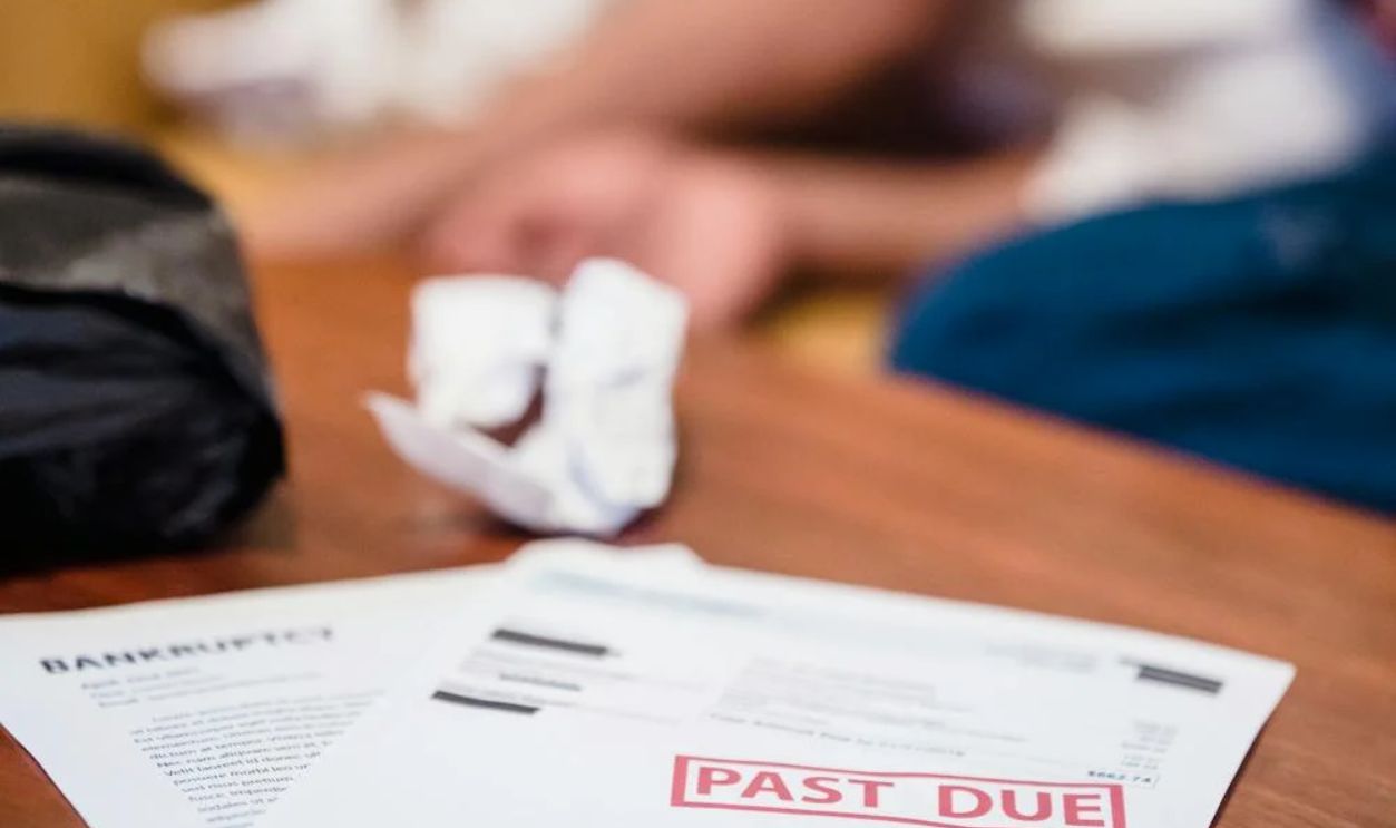 Unpaid Bills on a Table and a Distraught Man in Background