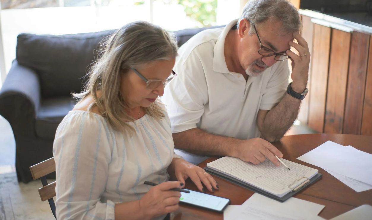 Elderly Couple Sitting at the Table with Documents and Using a Smartphone