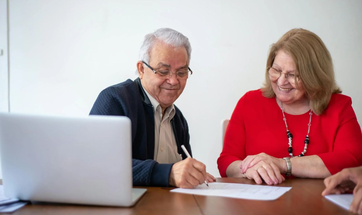 Man Writing on Paper Sitting Beside Woman in Red Blouse