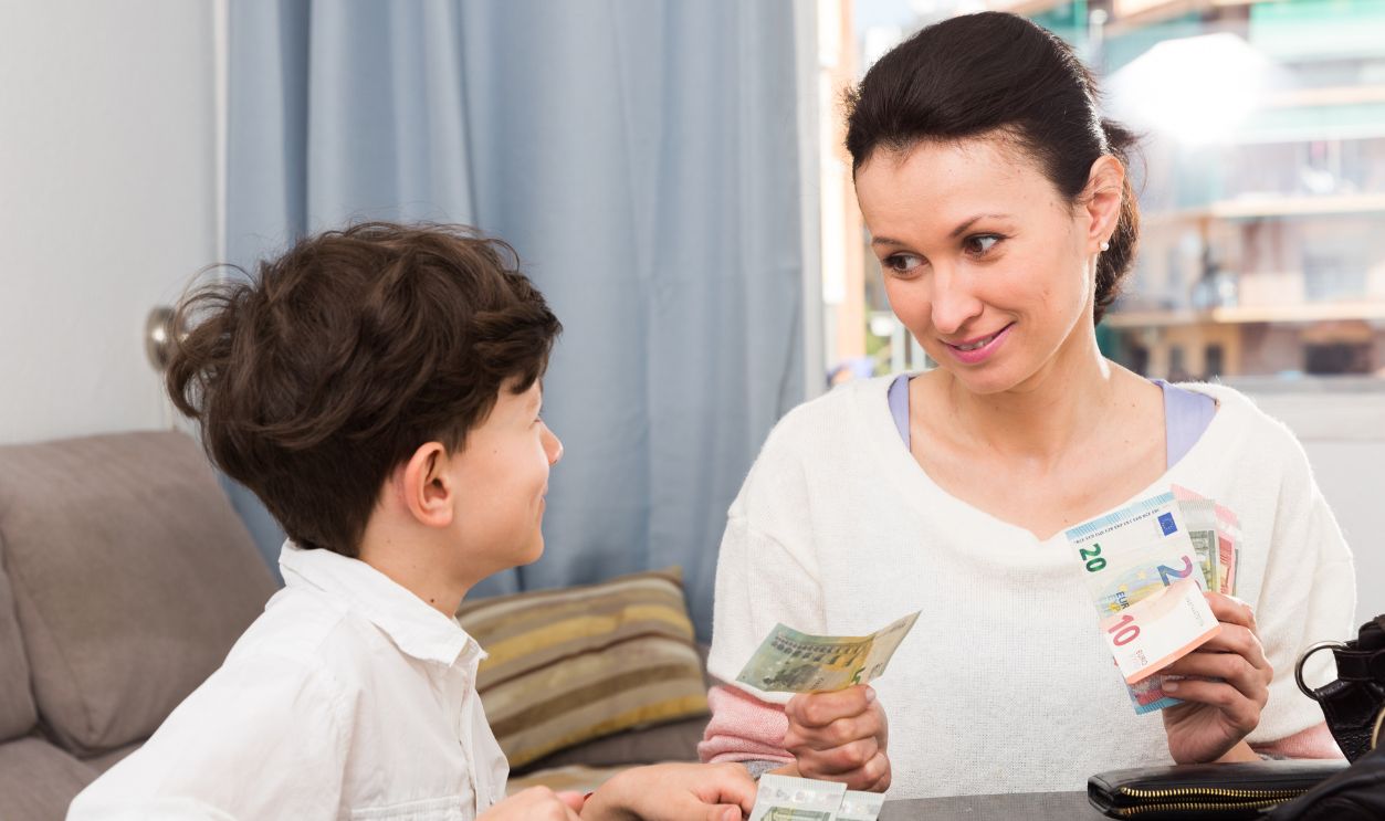 Portrait of positive woman giving money to teen boy in home interior