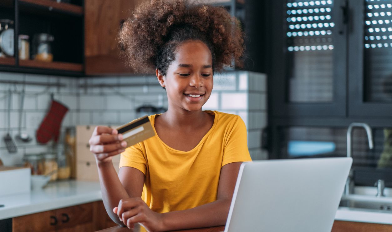 Shot of a smiling teenage girl holding a credit card and using a laptop at home.