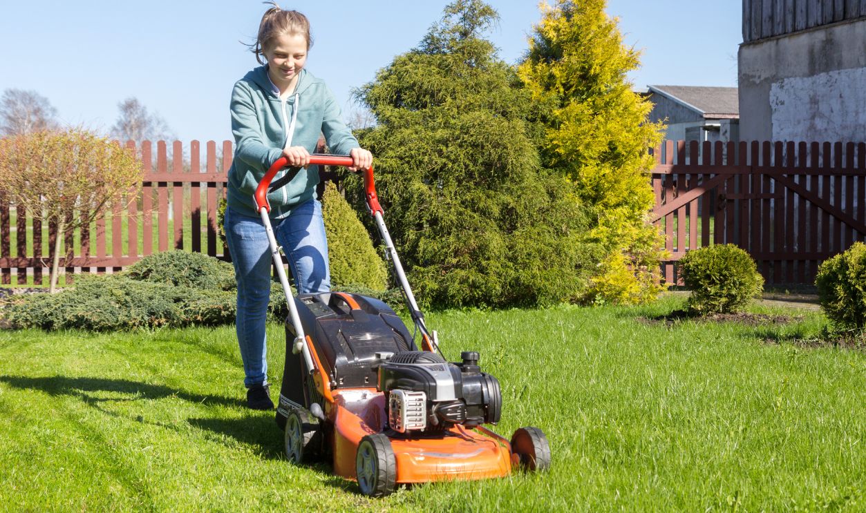 teenage girl working in garden, mowing grass with lawn-mower
