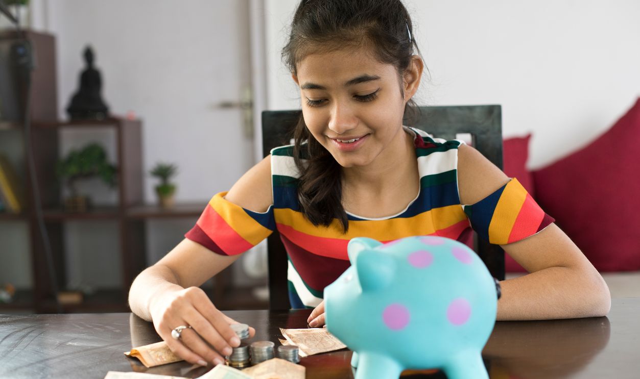 Girl with piggy bank and money on table