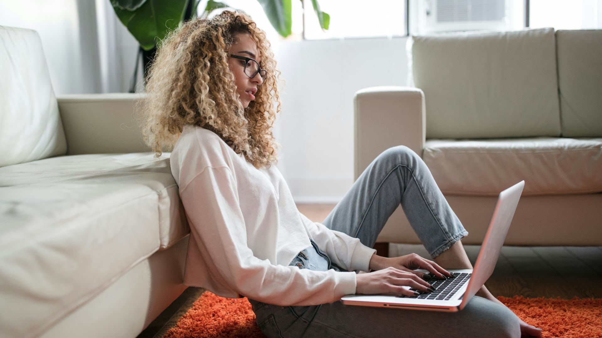 woman sitting on floor and leaning on couch using laptop