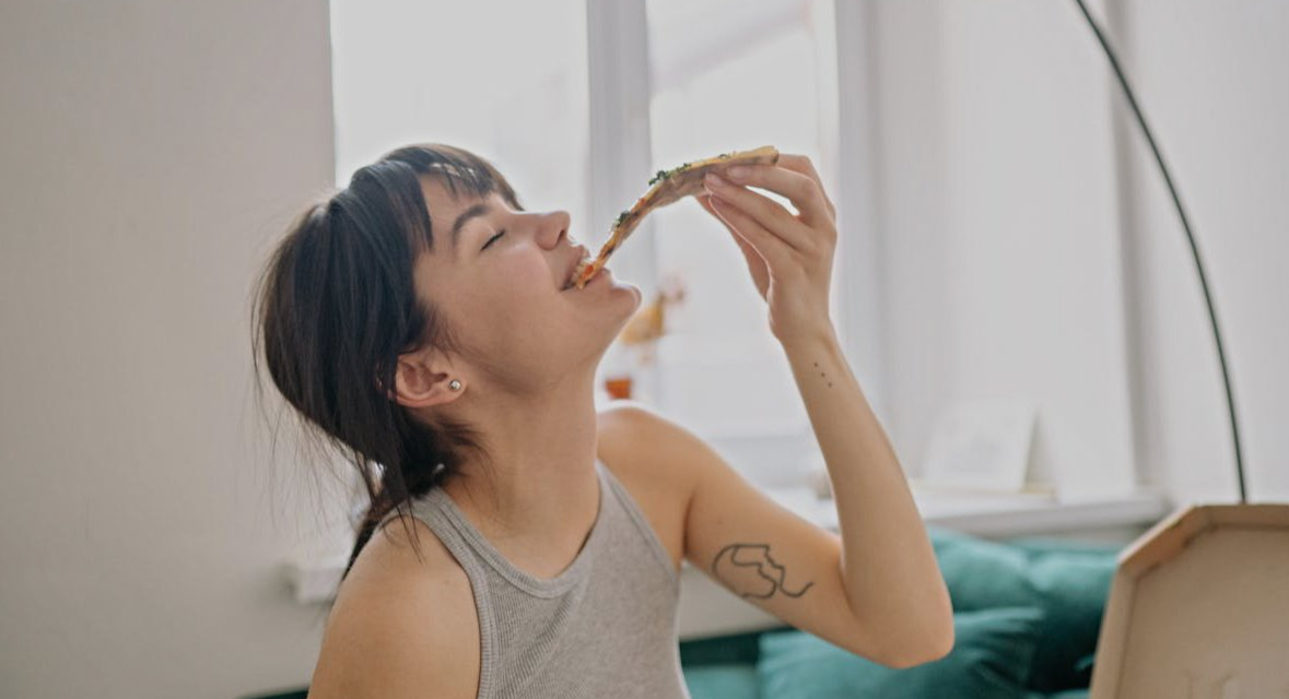 A Young Woman in Gray Tank Top Enjoying Eating Pizza