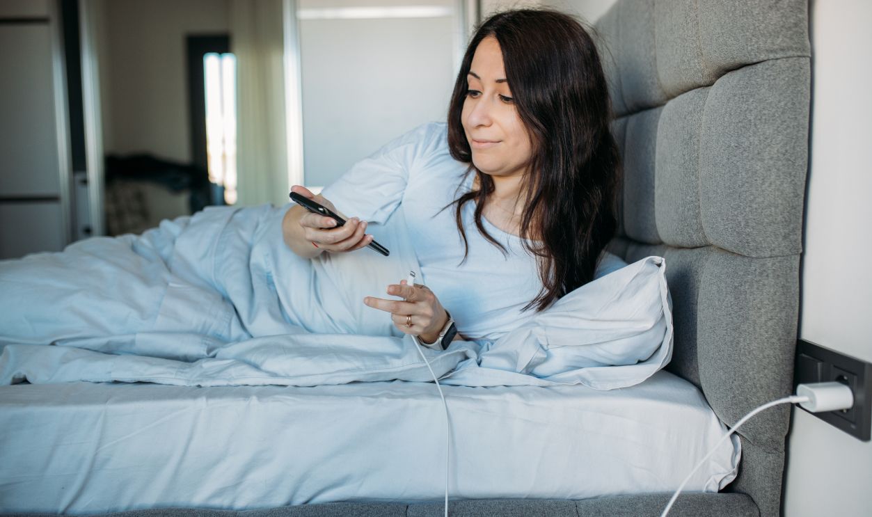 Woman inserting charging cable in smartphone when lying in bed