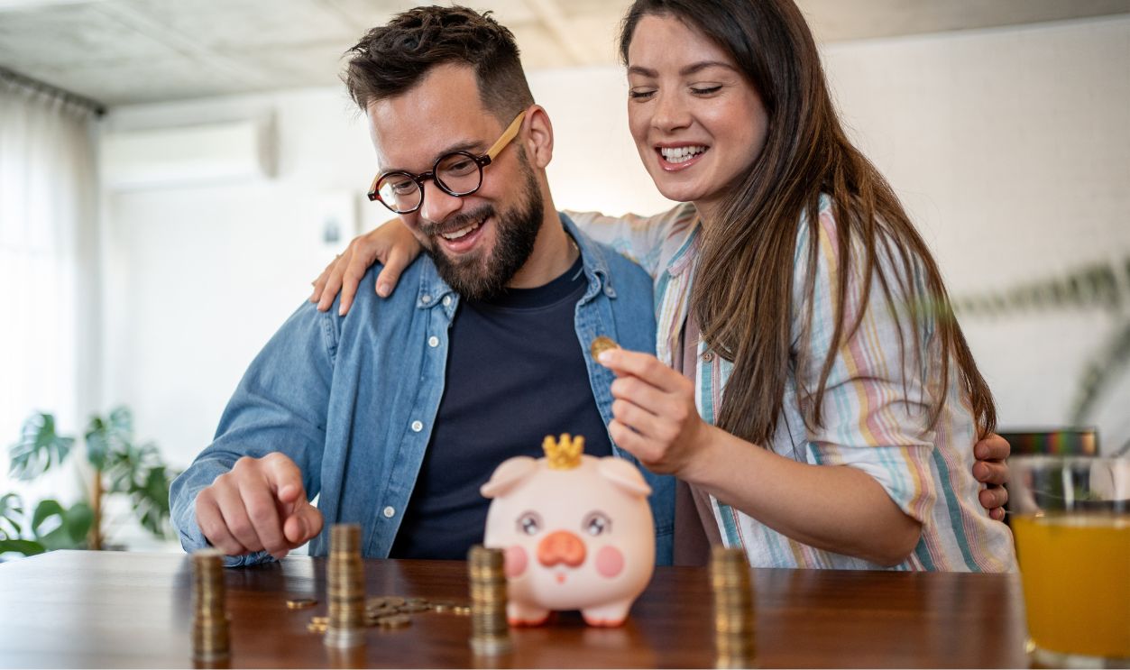 Young couple joyfully placing coins into a piggy bank, actively saving money for their future while enjoying the comfort of financial stability and planning for their dreams together