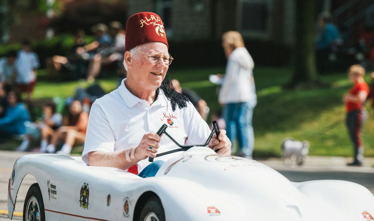 Elderly Man Driving Toy Car in Festival