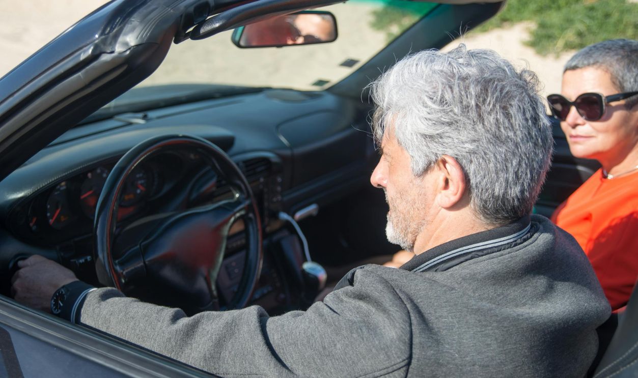 A Man Driving a Convertible Car with a Woman Wearing Sunglasses