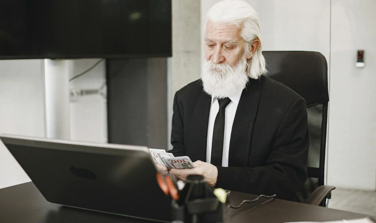 Elderly Man Counting Money in Office