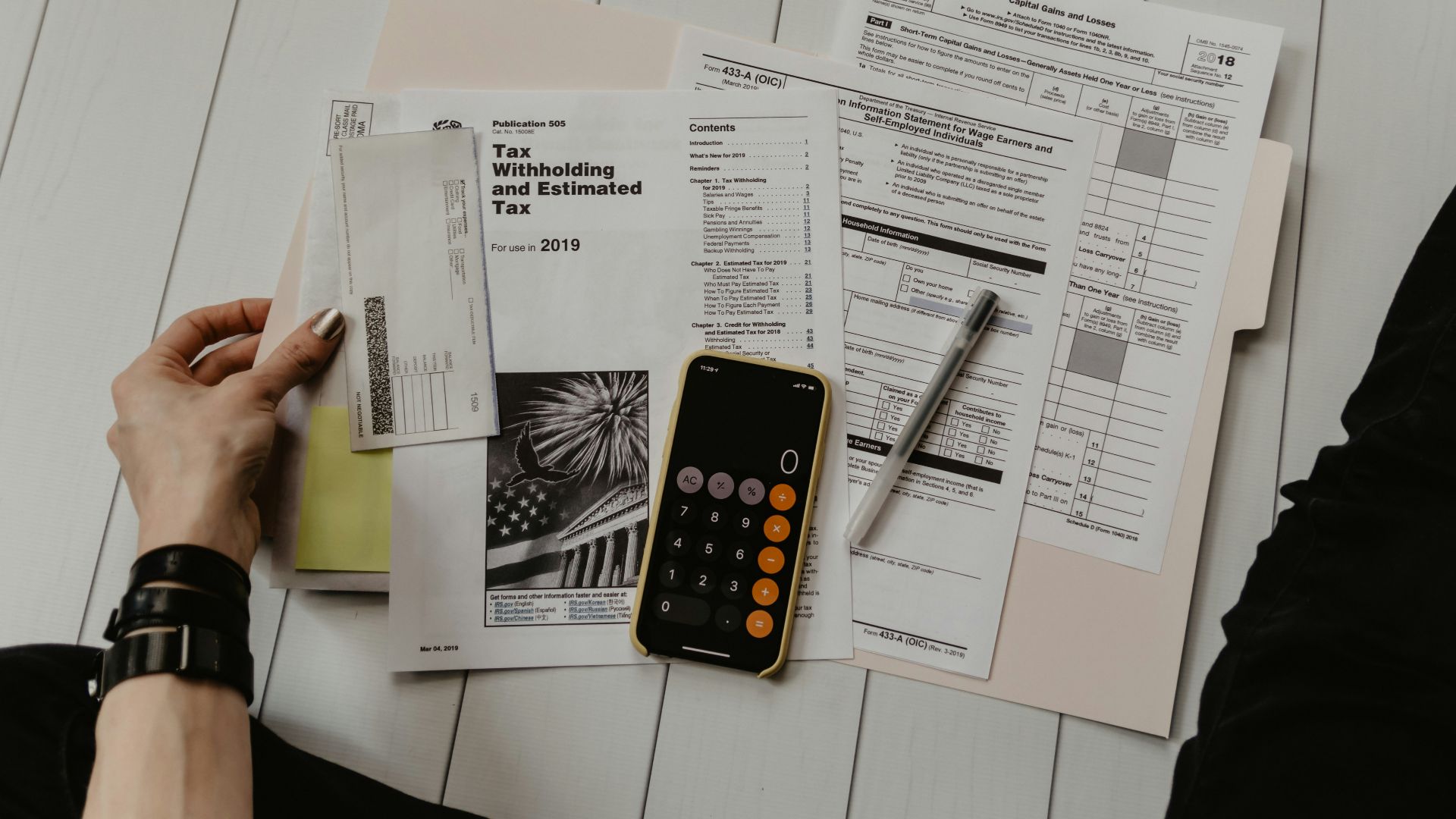 person holding paper near pen and calculator