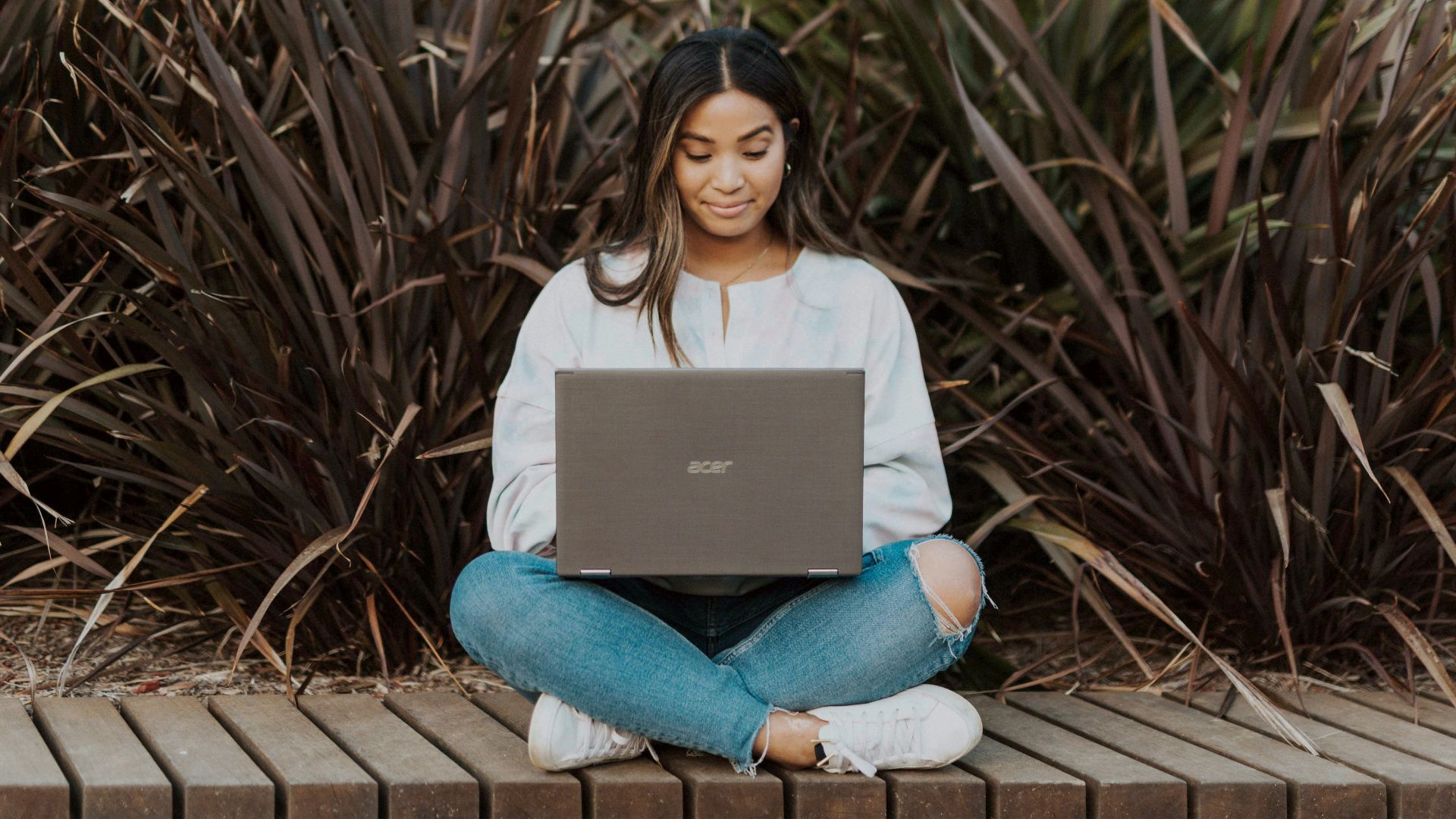 woman in white long sleeve shirt and blue denim jeans sitting on brown wooden pathway
