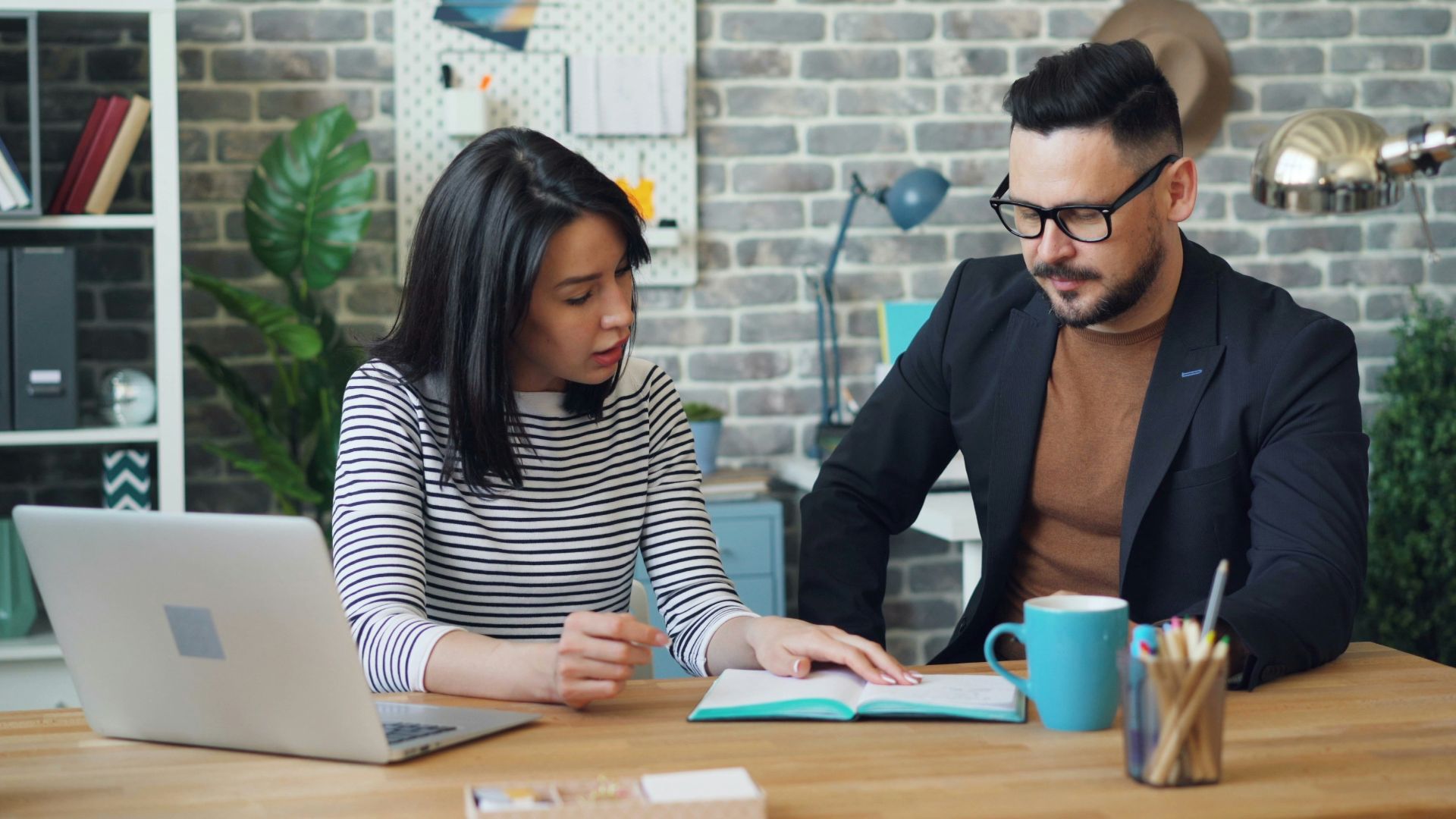 a man and a woman sitting at a table looking at a laptop