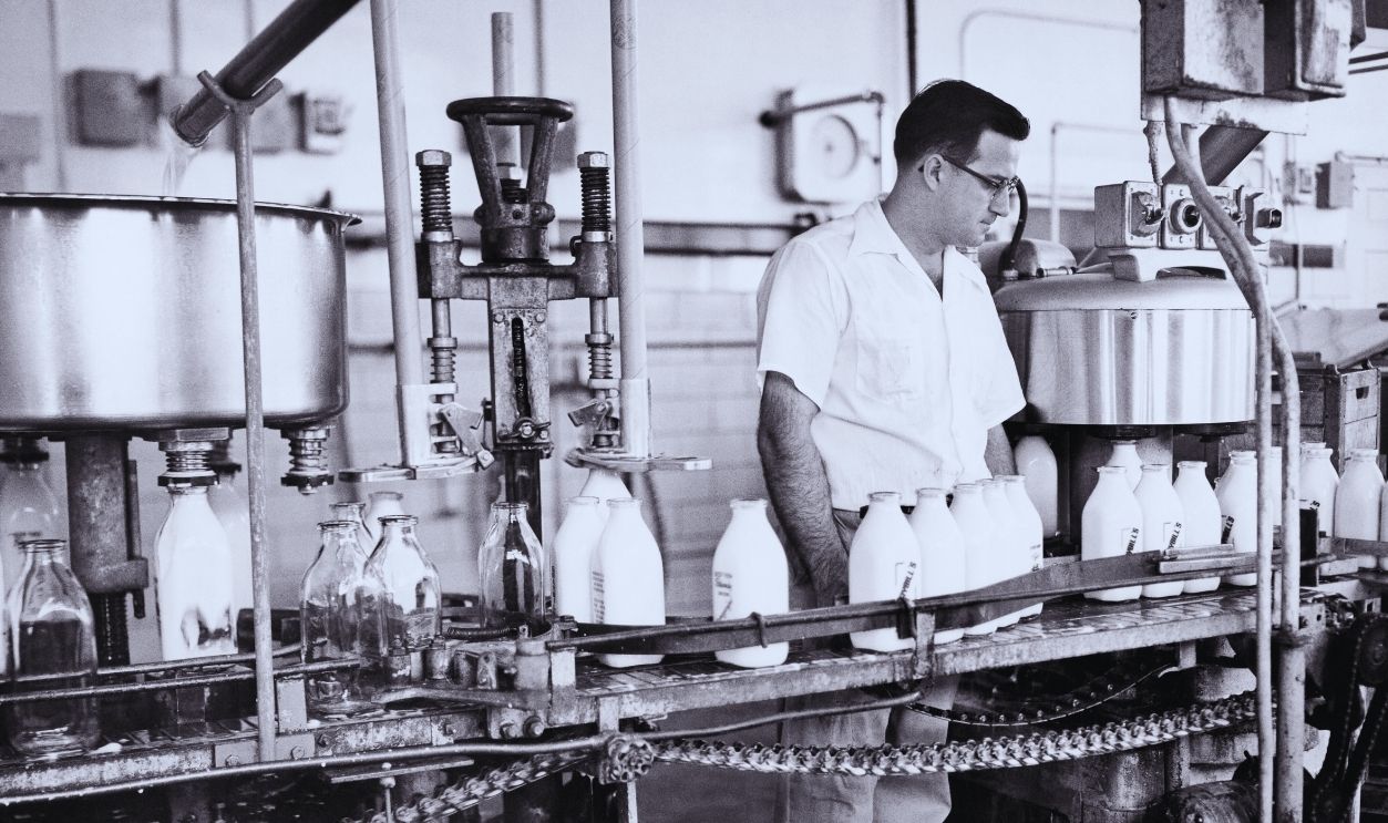 Gettyimages - 1248924030, Milk Assembly Line 1960s Quart Glass Milk Bottles Being Filled And Capped Man Employee Working On Food Processing Assembly Line In A Dairy