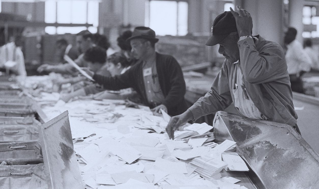 Gettyimages - 1318483857, Postal Employees Sort Mail View of postal employees as they hand-sort mail on table, March 1, 1966.